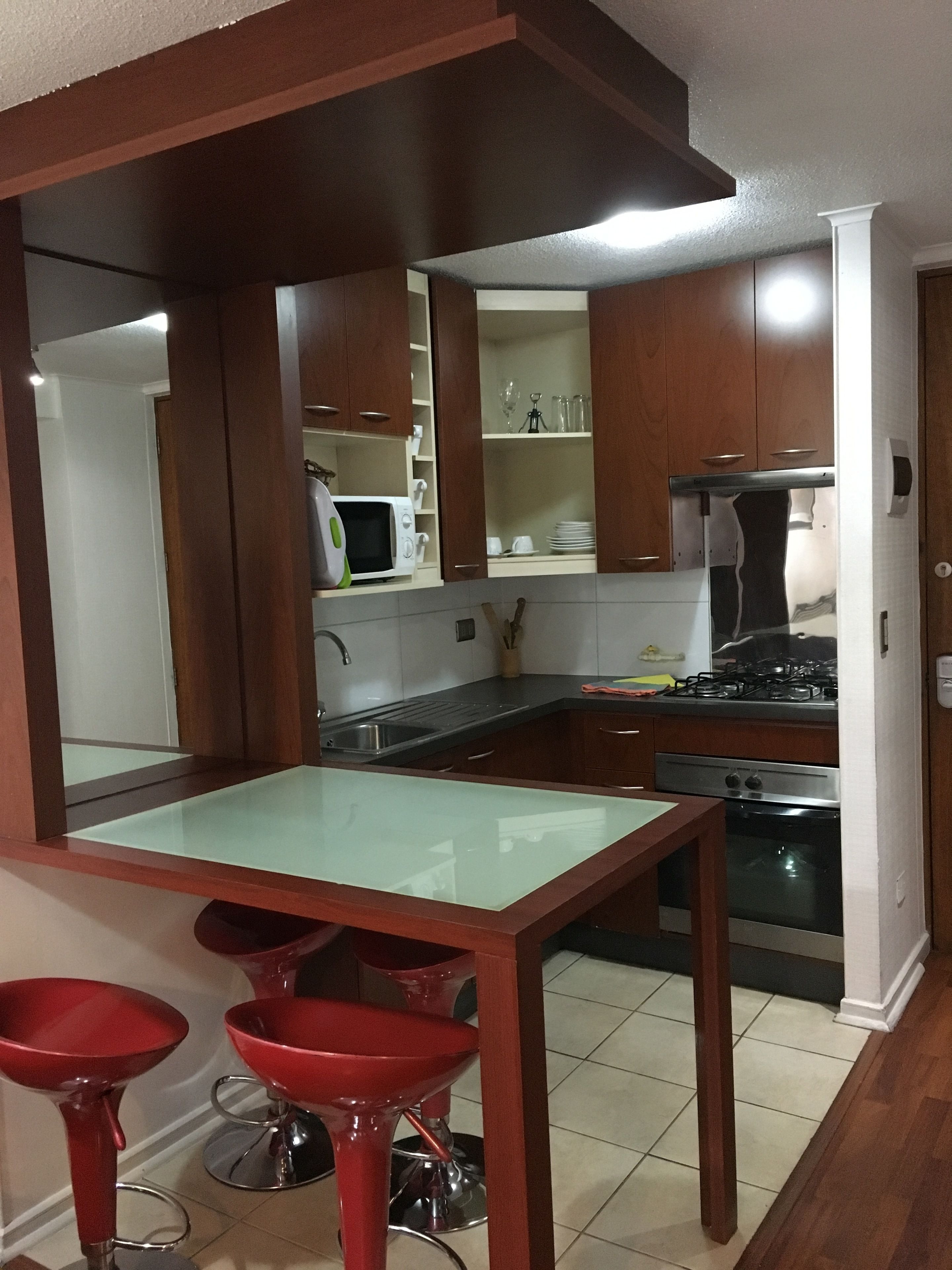 A kitchen with wooden cabinets, a microwave, a gas stove, and a glass-top dining table with red bar stools.