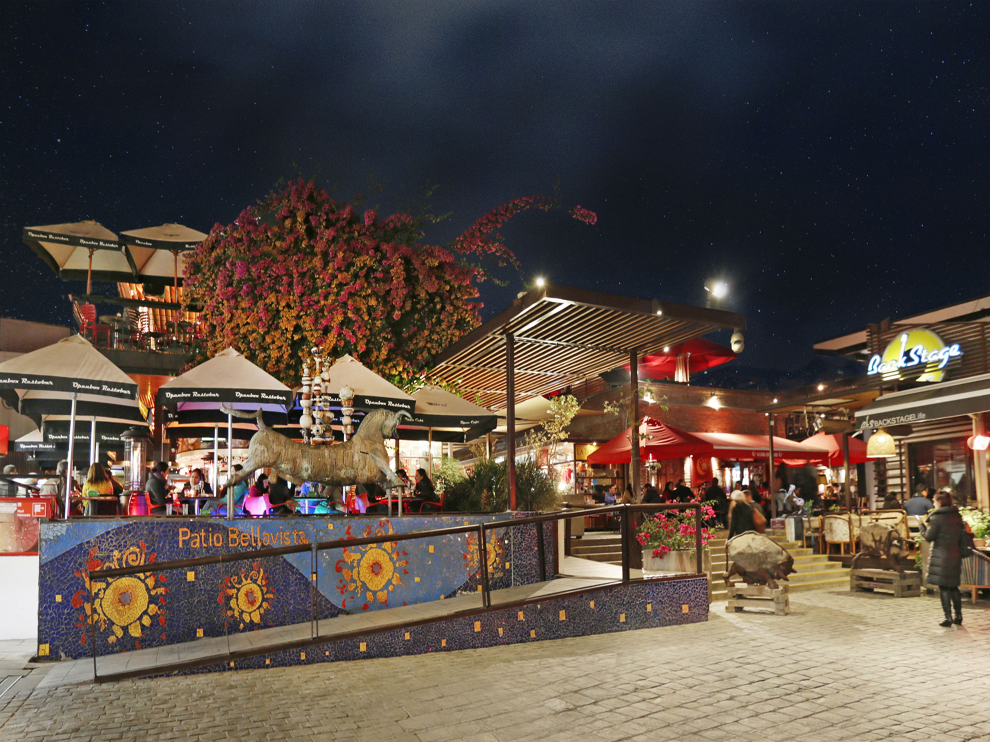 Una plaza al aire libre con una fuente decorativa, zonas de descanso y diversas opciones de restaurantes.