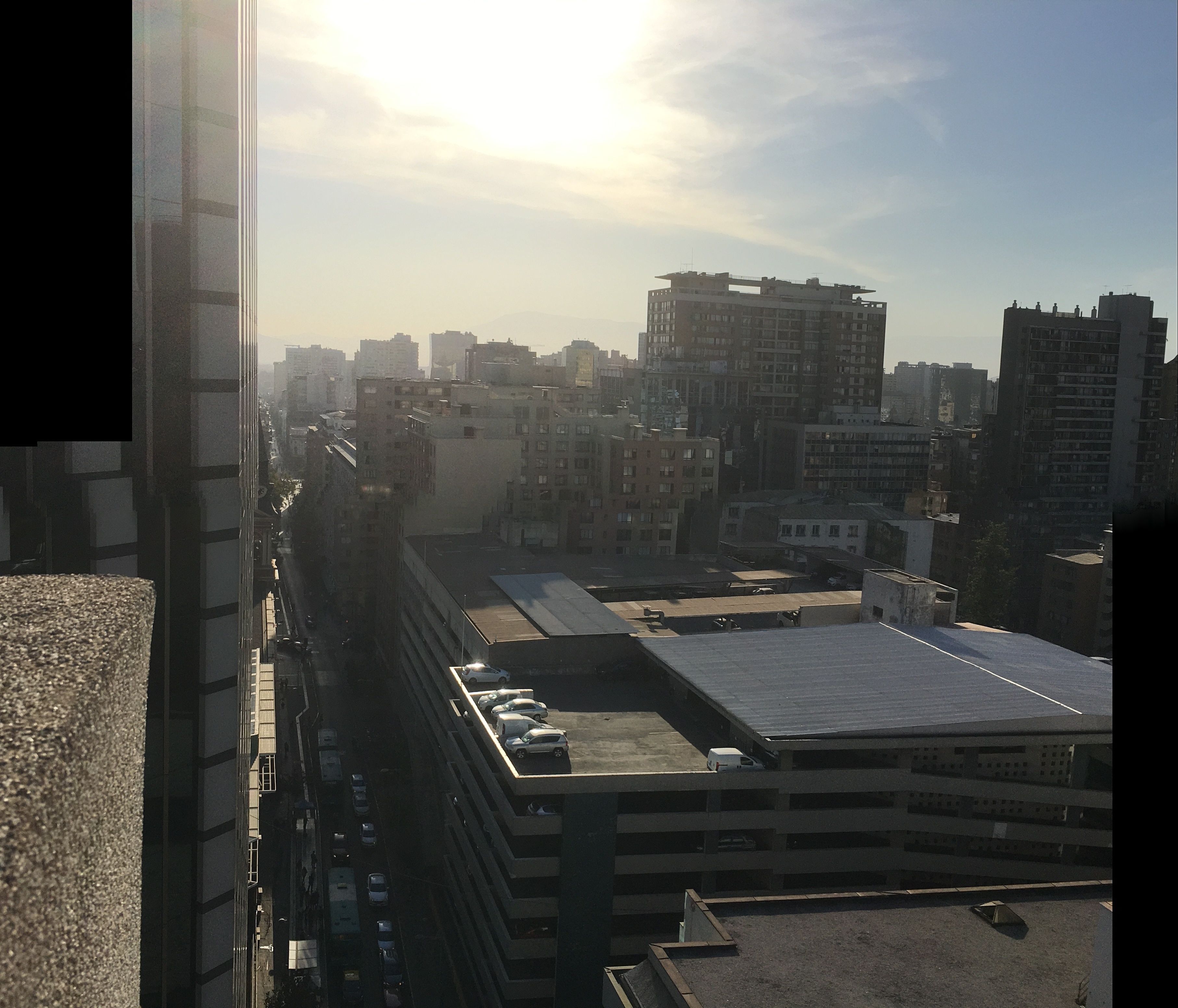 A high-rise building with multiple floors, a parking garage below, and a view of other buildings in the distance.