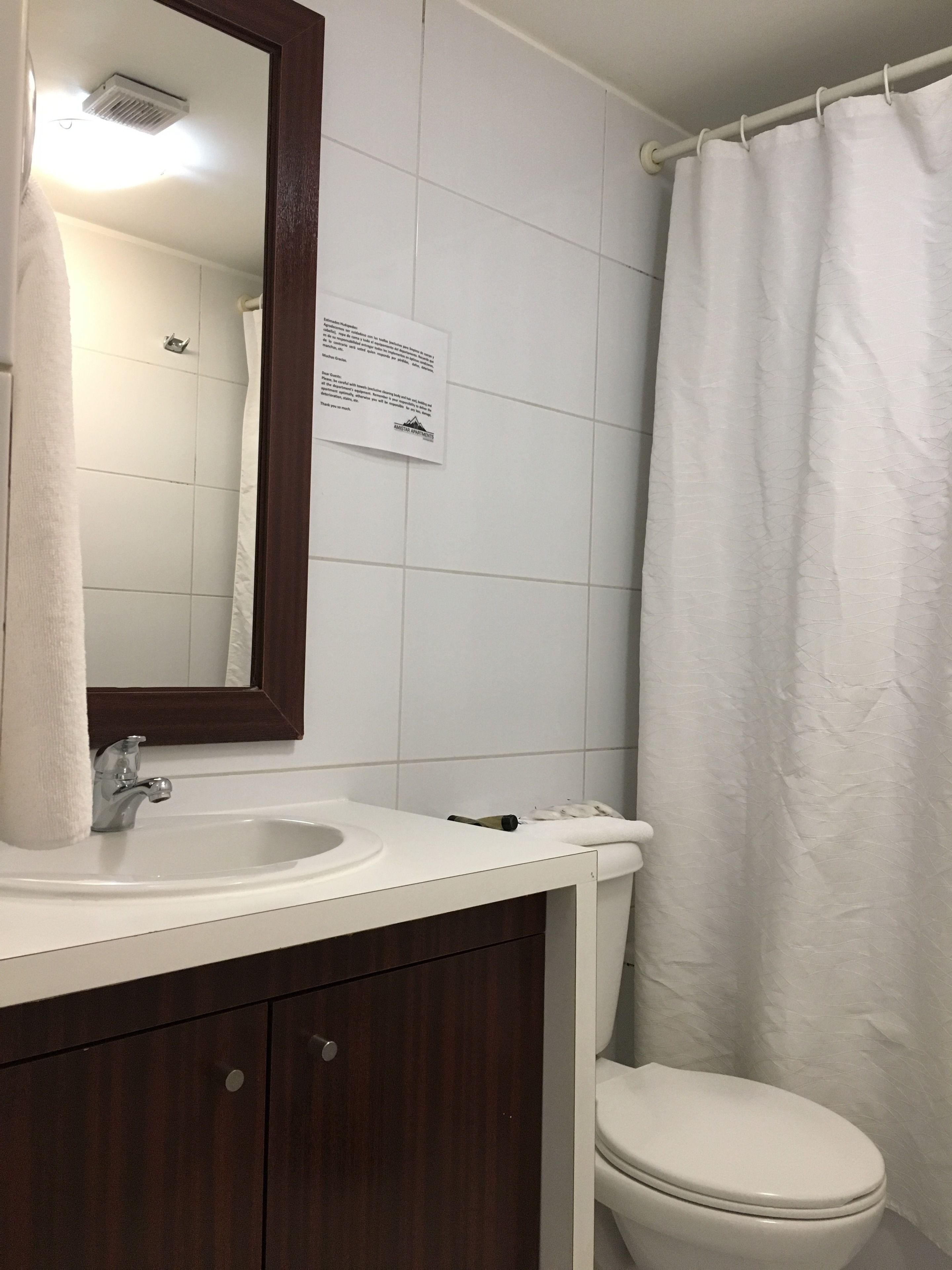 Un baño con lavamanos blanco, espejo, inodoro y cortina de ducha.