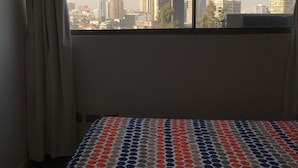 A hotel room with a bed, a window with curtains, and a view of a cityscape and mountains. - Amistar Apartments (Santiago)