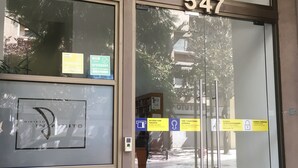 A building entrance with a glass door, a number sign, and various signs indicating access with a card, a pull handle, and a closed door. - Amistar Apartments (Santiago)
