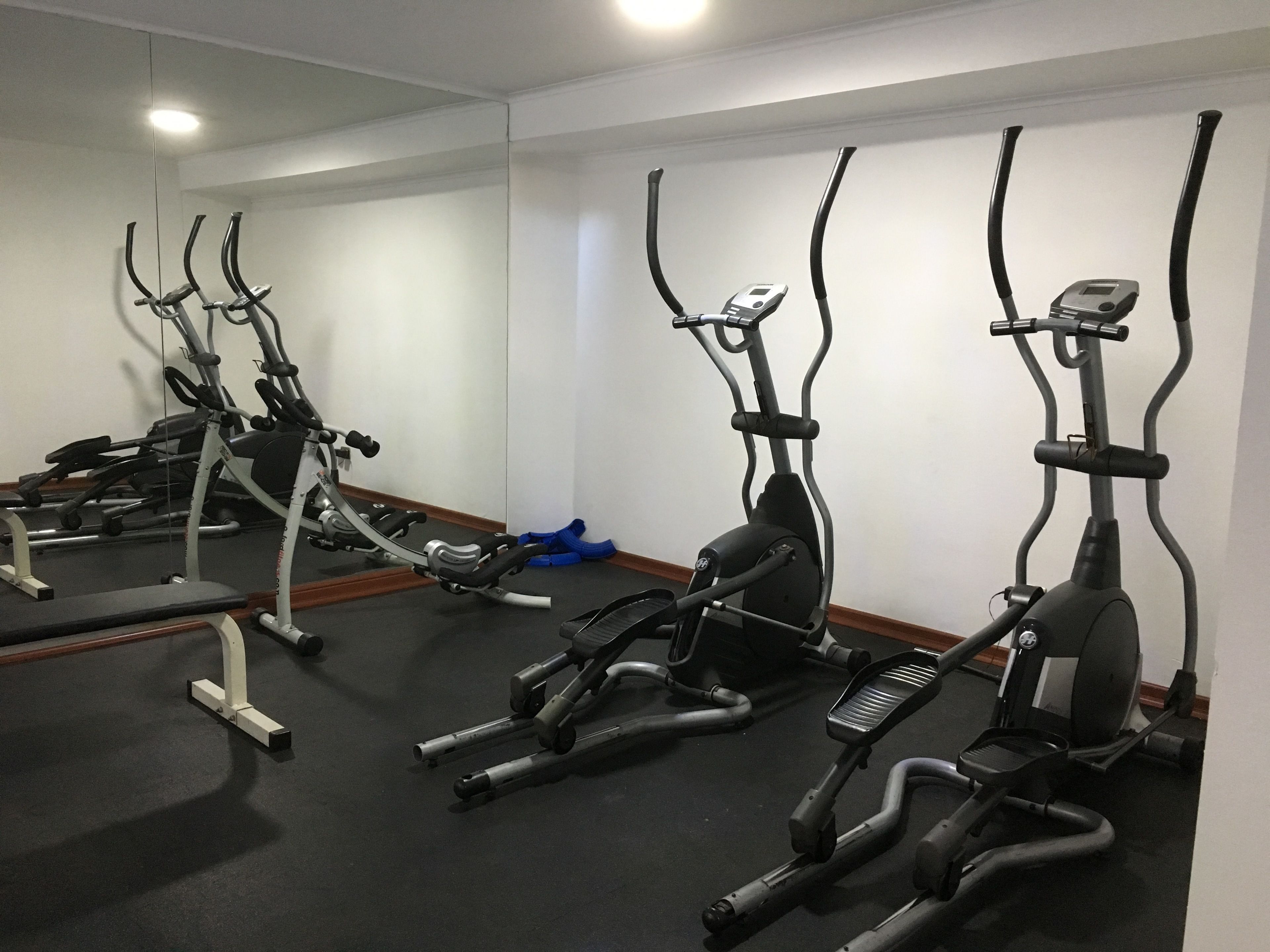 A gym with multiple exercise machines, including ellipticals and a bench.
