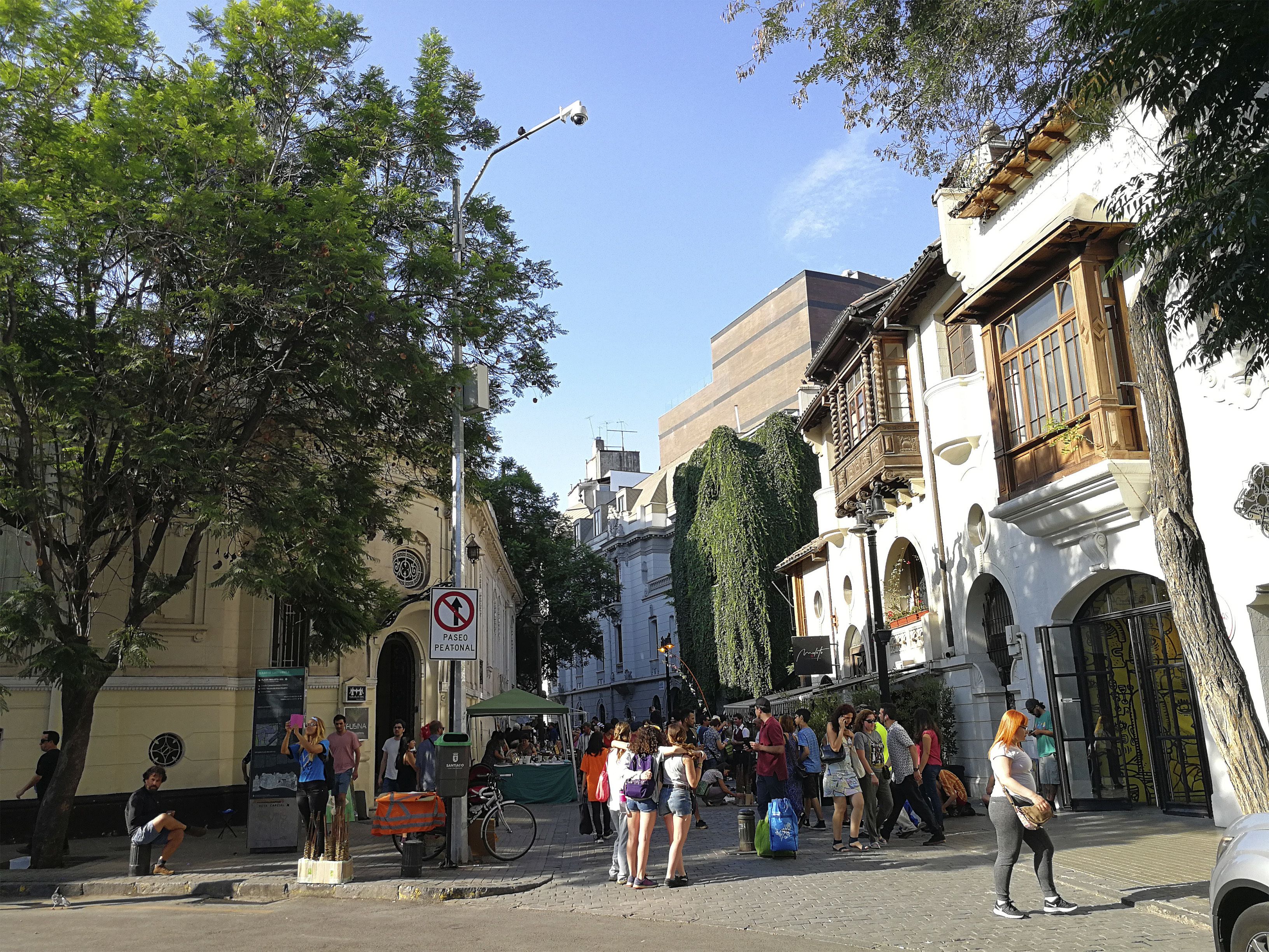 A bustling street scene with pedestrians, a market stall, and historic buildings.