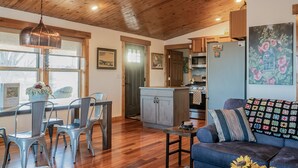 A spacious living room with a wooden ceiling, a dining area with metal chairs, a blue sofa with a colorful cushion, and a kitchen area with wooden cabinets and a refrigerator. - Minutes to Galena.  Bird Cottage @ Sorriso Vineyard Galena Illinois (Galena)