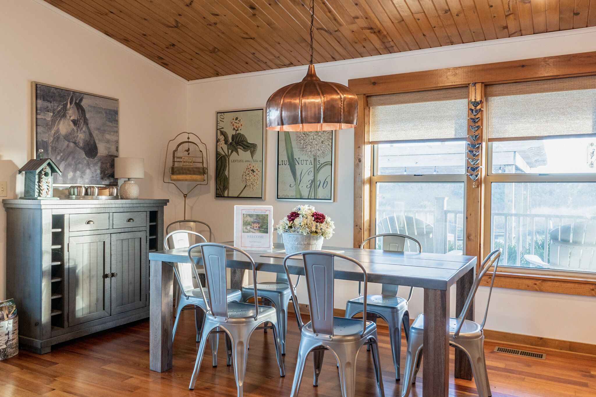 Un espace repas doté d’un plafond en bois, d’une table avec des chaises, d’un luminaire suspendu et d’œuvres d’art accrochées aux murs.