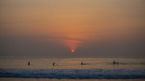 A sunset over the ocean with three people in the water.