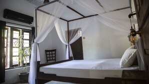 A room with a four-poster bed, a potted plant, a wooden chair, and a window with curtains.