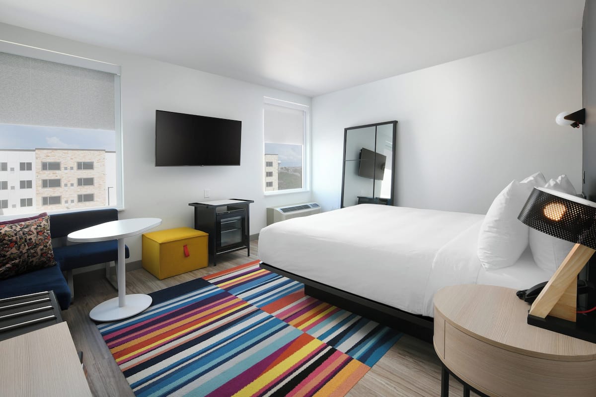 Una moderna camera d'albergo con un letto grande, una TV a schermo piatto, una piccola scrivania e un tappeto colorato a righe.