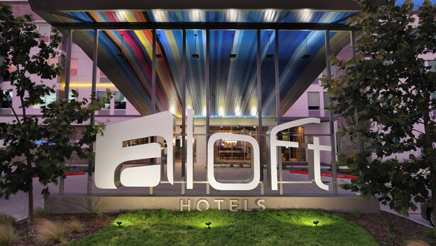 A modern hotel entrance with a large illuminated sign, a glass facade, and a well-maintained lawn. - Aloft by Marriott Austin Round Rock (Round Rock)
