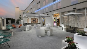 A modern outdoor seating area with white and green chairs, white tables, and umbrellas. - Aloft by Marriott Austin Round Rock (Round Rock)