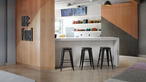 A modern kitchen with a wooden accent wall, a white countertop, and three black stools. - Aloft by Marriott Austin Round Rock (Round Rock)