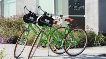 Dos bicicletas verdes con ruedas marrones estacionadas frente a un edificio con un letrero que dice "element by Westin".