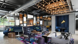 A modern lounge area with seating, a patterned rug, and a neon sign on the wall. - Aloft by Marriott Austin Round Rock (Round Rock)