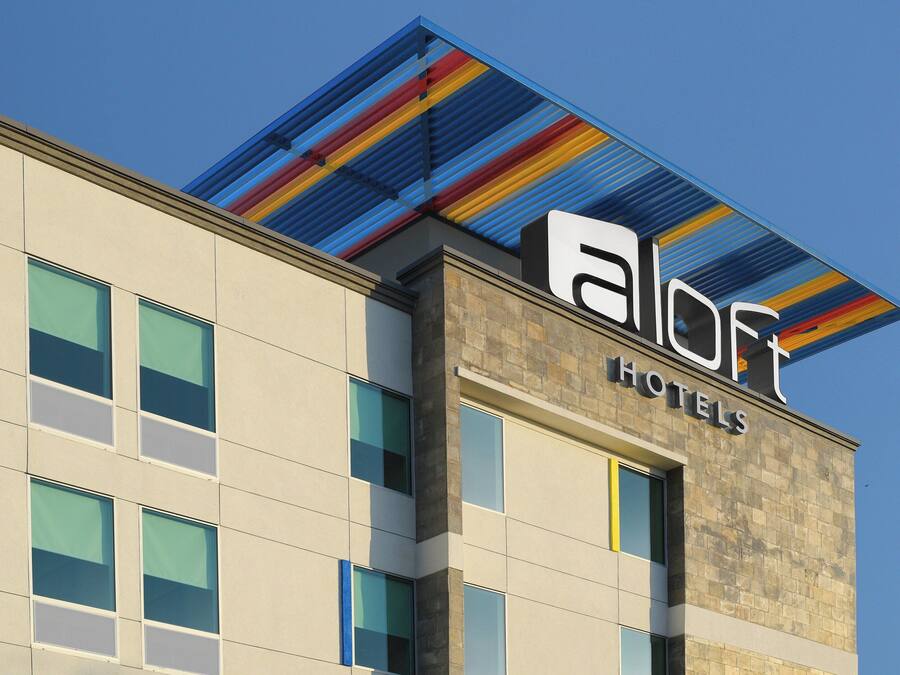 Ein Hotelgebäude mit modernem Design, das ein gut sichtbares Logo und den Namen im Eingangsbereich zeigt.