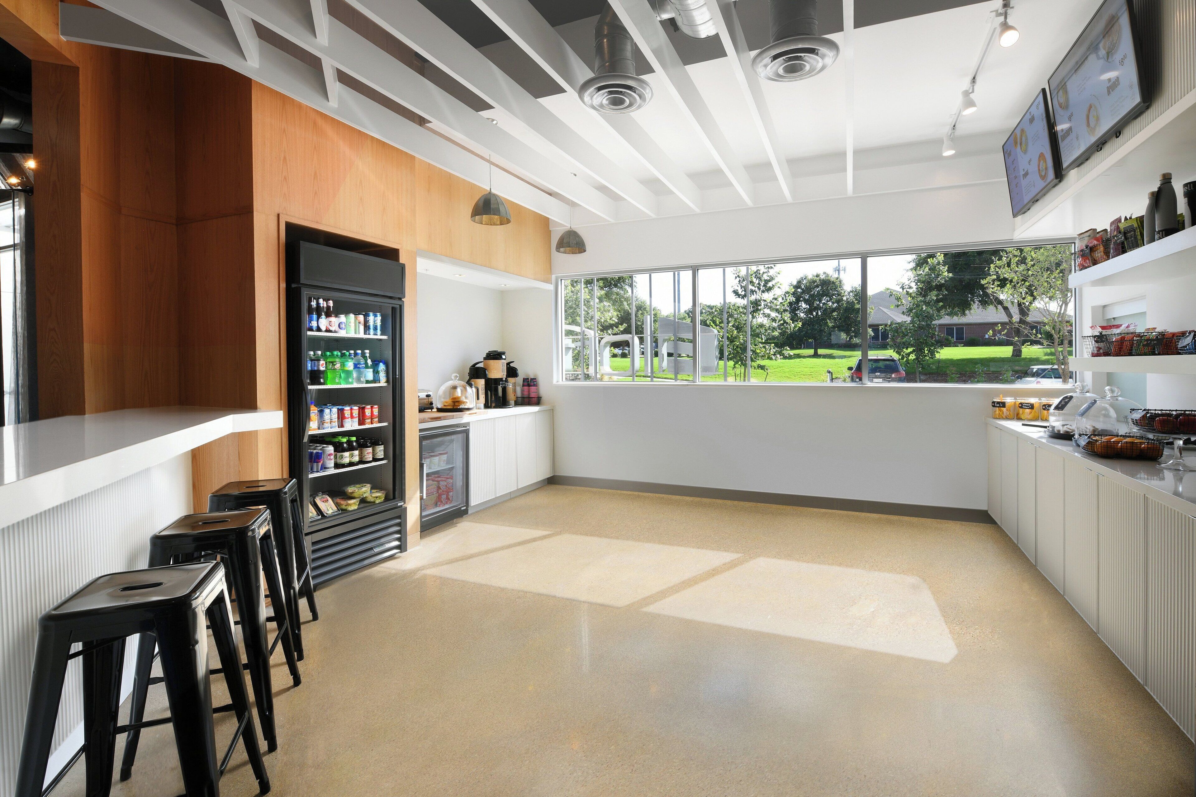 A modern bar area with stools, a refrigerator stocked with beverages, and a view of the outdoors.