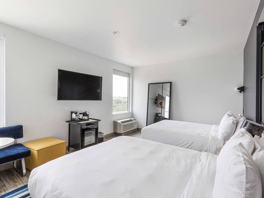 A hotel room with two beds, a desk, a chair, a TV, and a window.