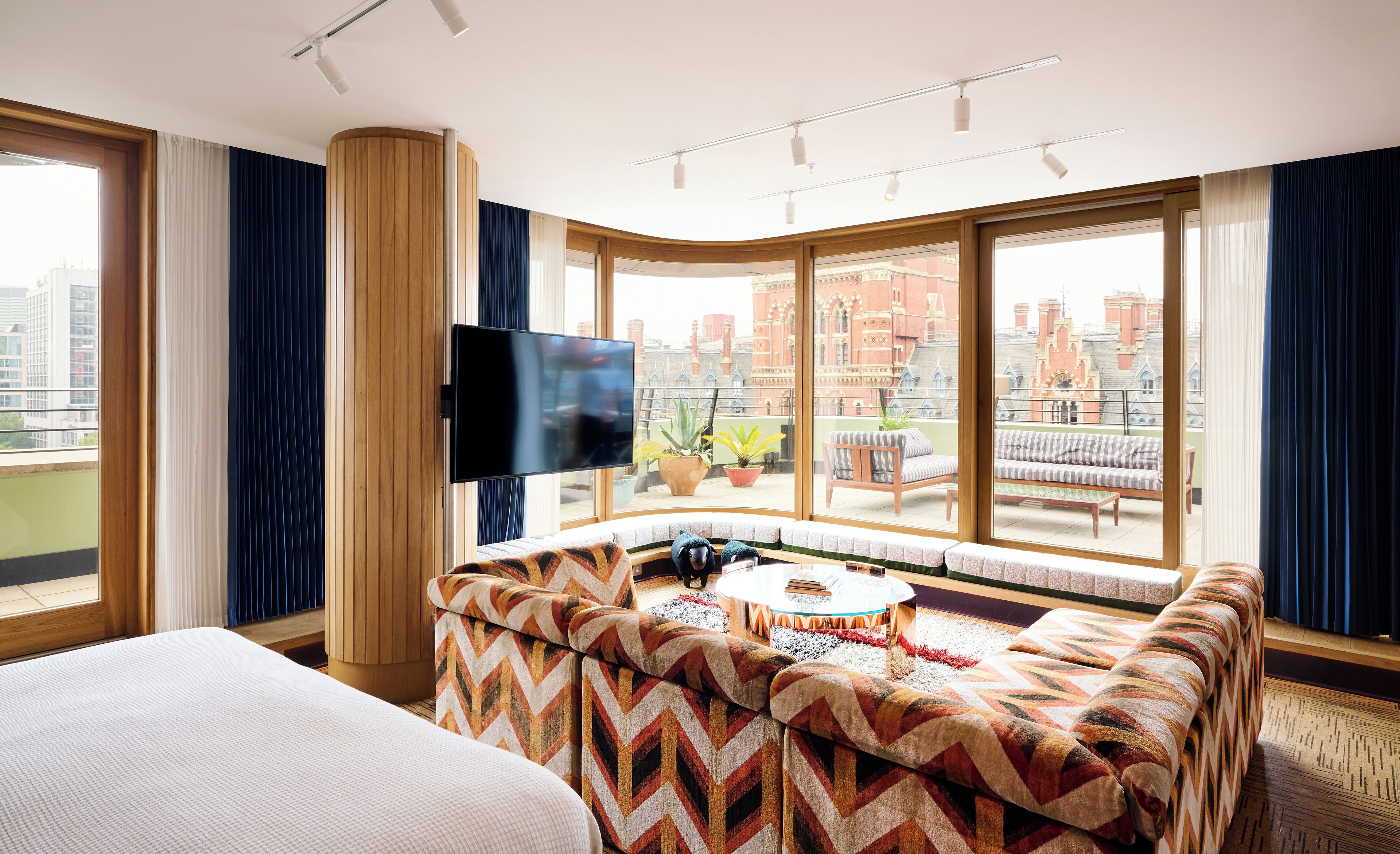 Habitación de hotel moderna con un ventanal grande, un televisor de pantalla plana, un sofá y una mesita.
