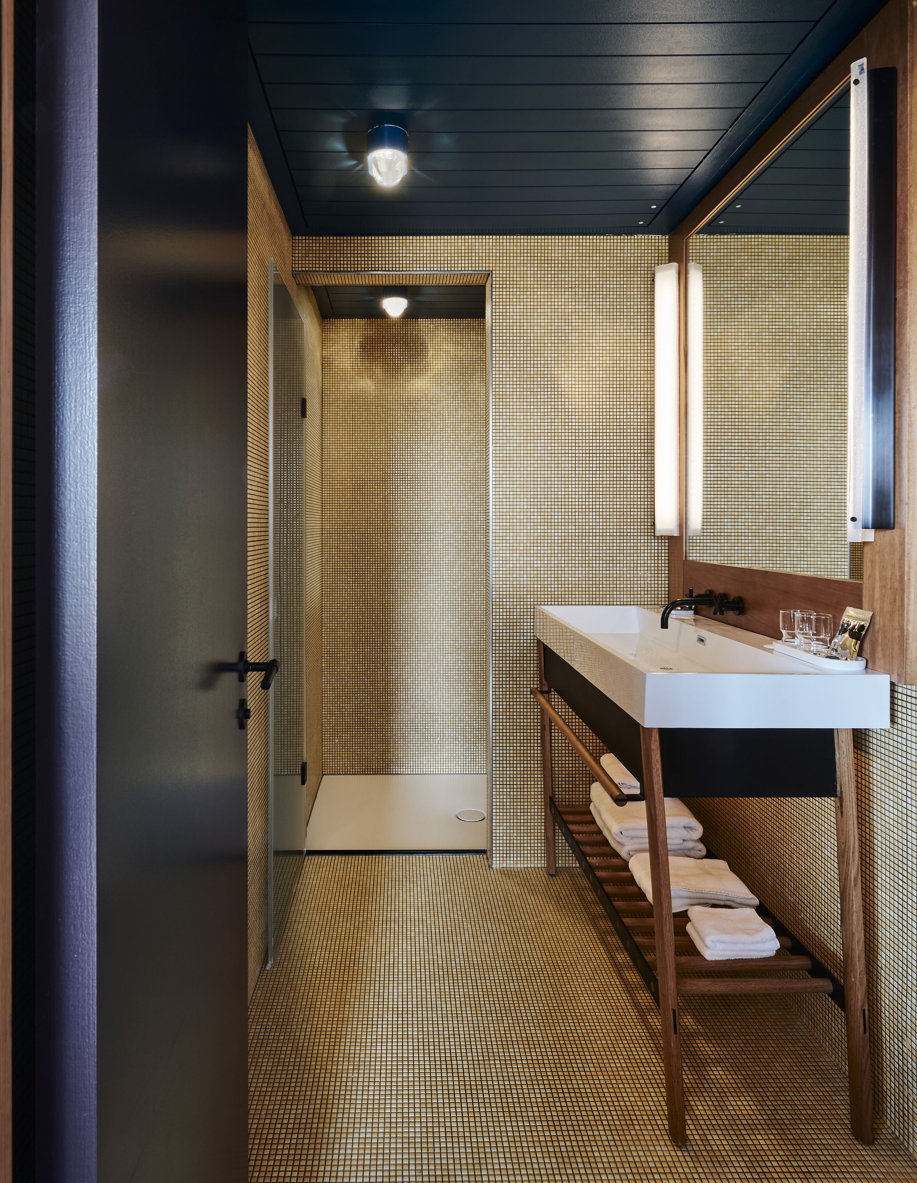 Un baño con piso de baldosas, lavamanos, espejo y zona de ducha.