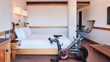 Hotelkamer met een bed, een bureau, een stoel, een zithoogte verstelbaar bureau, een laptop en een hometrainer.