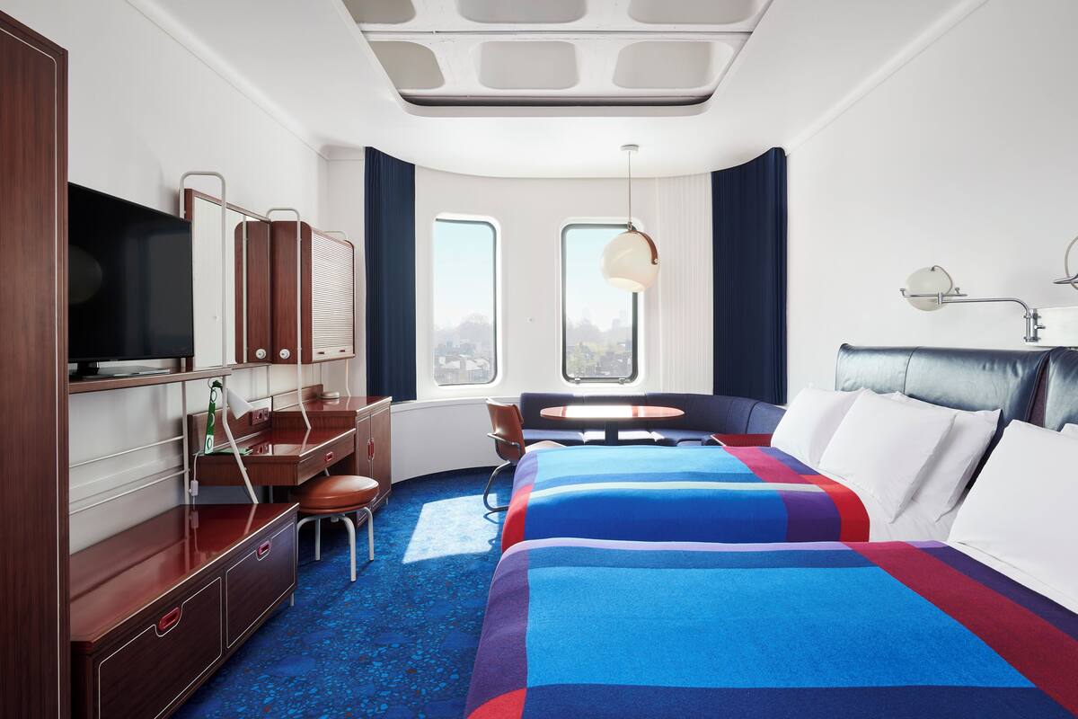 A modern hotel room with a large bed, a desk with a chair, a television, and a window with curtains.