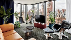 Ein modernes Wohnzimmer mit einem großen Fenster, Ledersofas, einem Flachbildfernseher und verschiedenen Pflanzen.