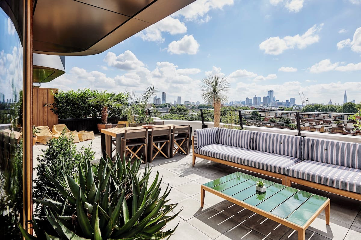 A rooftop terrace with a sofa, tables, and chairs, overlooking a city skyline.