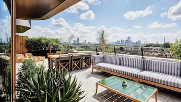 Terraço no telhado com sofá, mesas e cadeiras, com vista para o horizonte urbano.