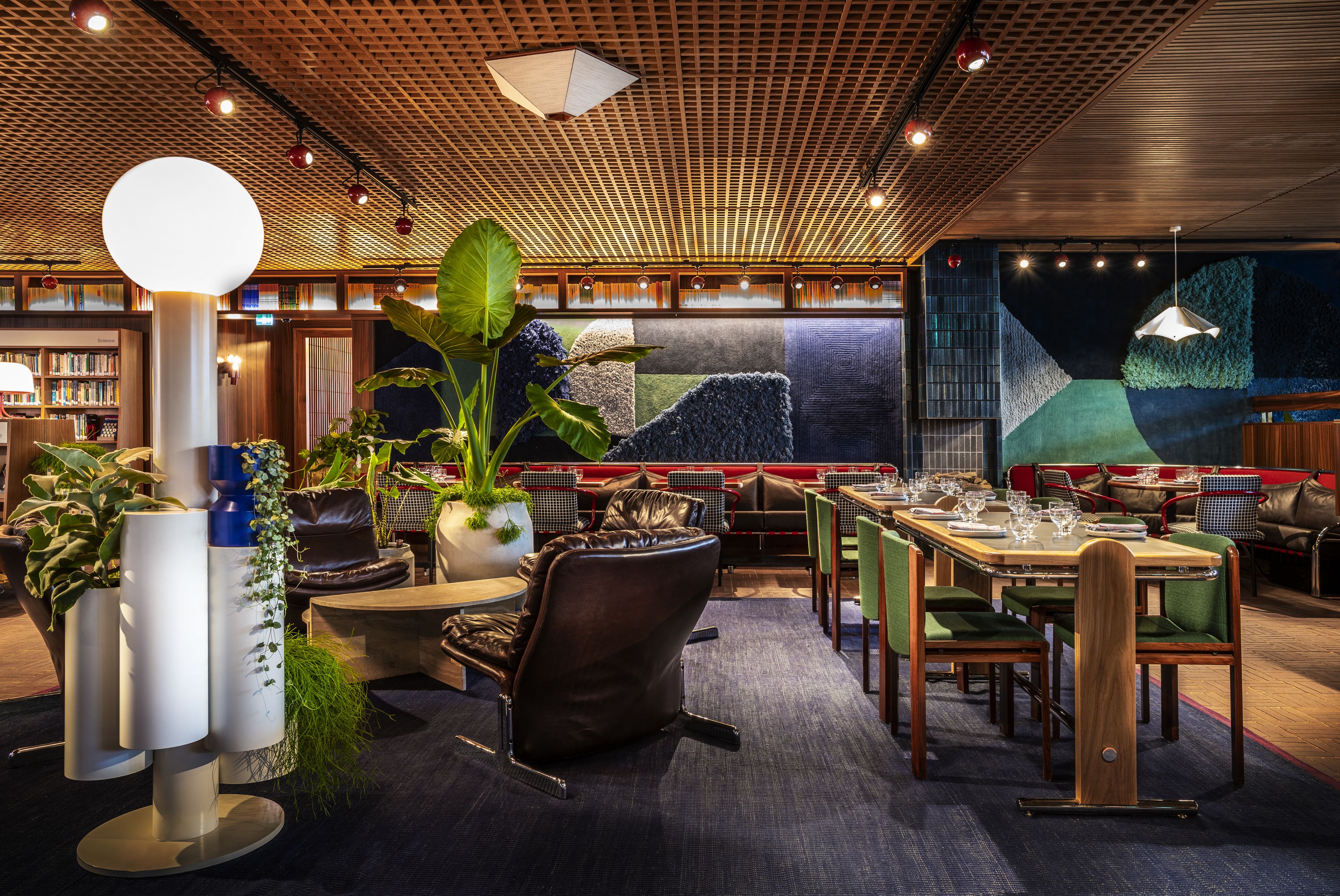 A restaurant with a modern design, featuring a wooden ceiling, green upholstered chairs, and a large mural on the back wall.