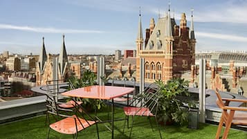 A rooftop terrace with a table and chairs, a view of a historic building, and a cityscape in the background.