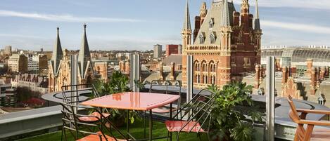 Una terraza en la azotea con una mesa y sillas, vistas de un edificio histórico y un paisaje urbano de fondo.