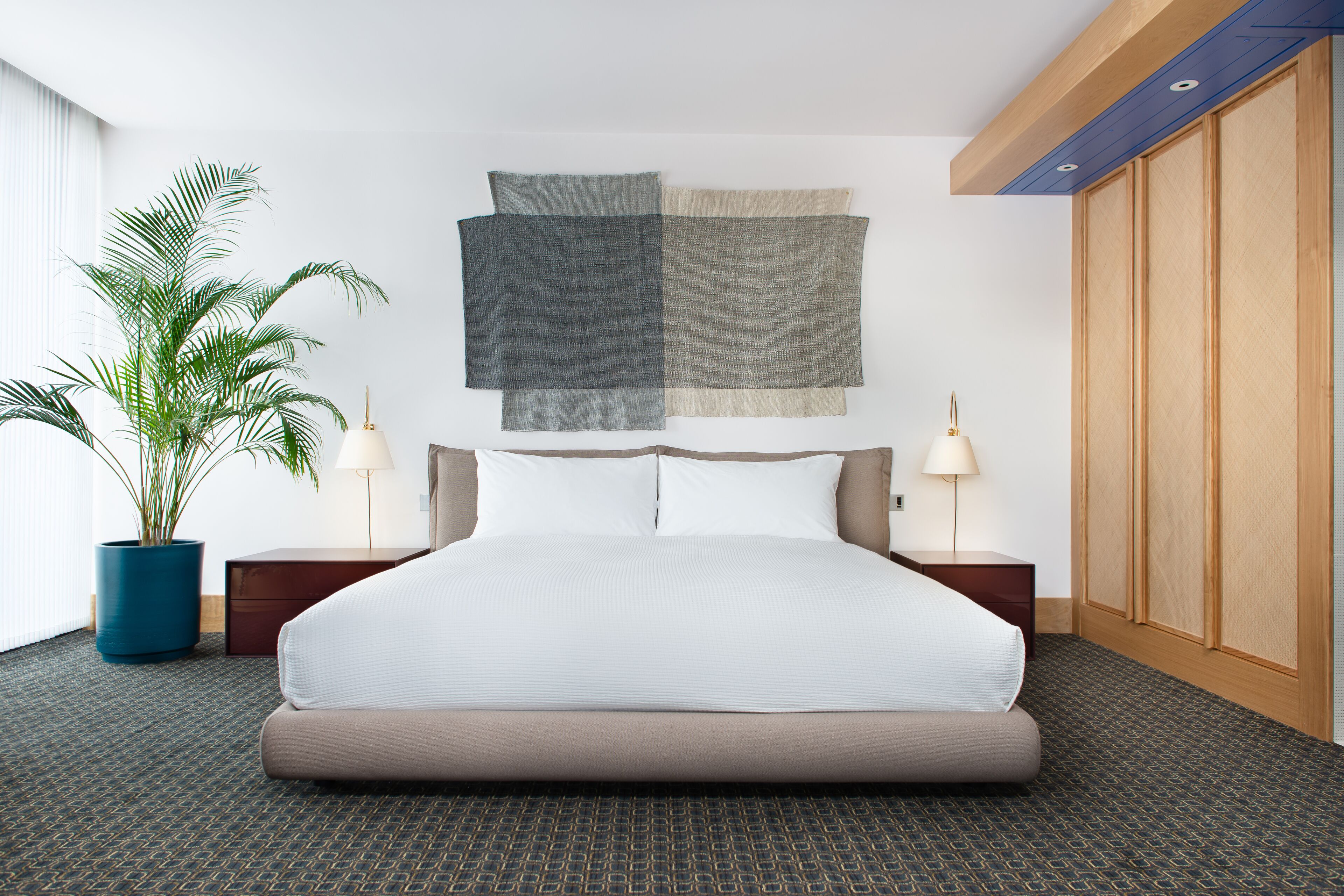 Ein modernes Hotelzimmer mit einem großen Bett, zwei Nachttischen, einer Zimmerpflanze und einem Wandbild.
