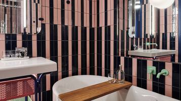 Une salle de bain moderne avec des carreaux noirs et roses à rayures, un lavabo blanc, un miroir et une étagère en bois.