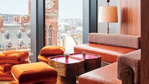 Ein modernes Zimmer mit großem Fenster, Blick auf einen Glockenturm und einer gemütlichen Sitzecke mit Lampe.