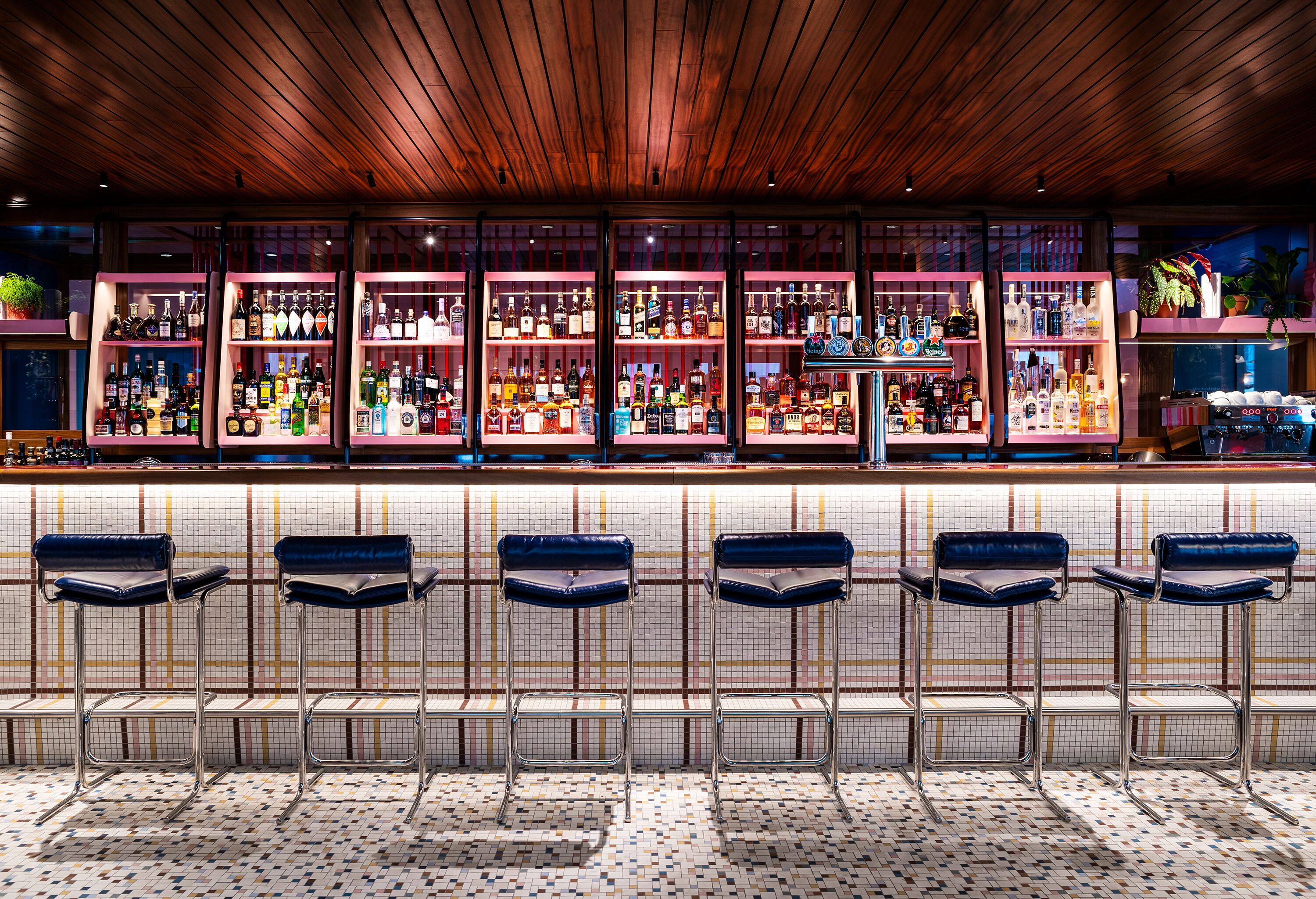 A bar area with multiple shelves of bottles, bar stools, and a patterned floor.