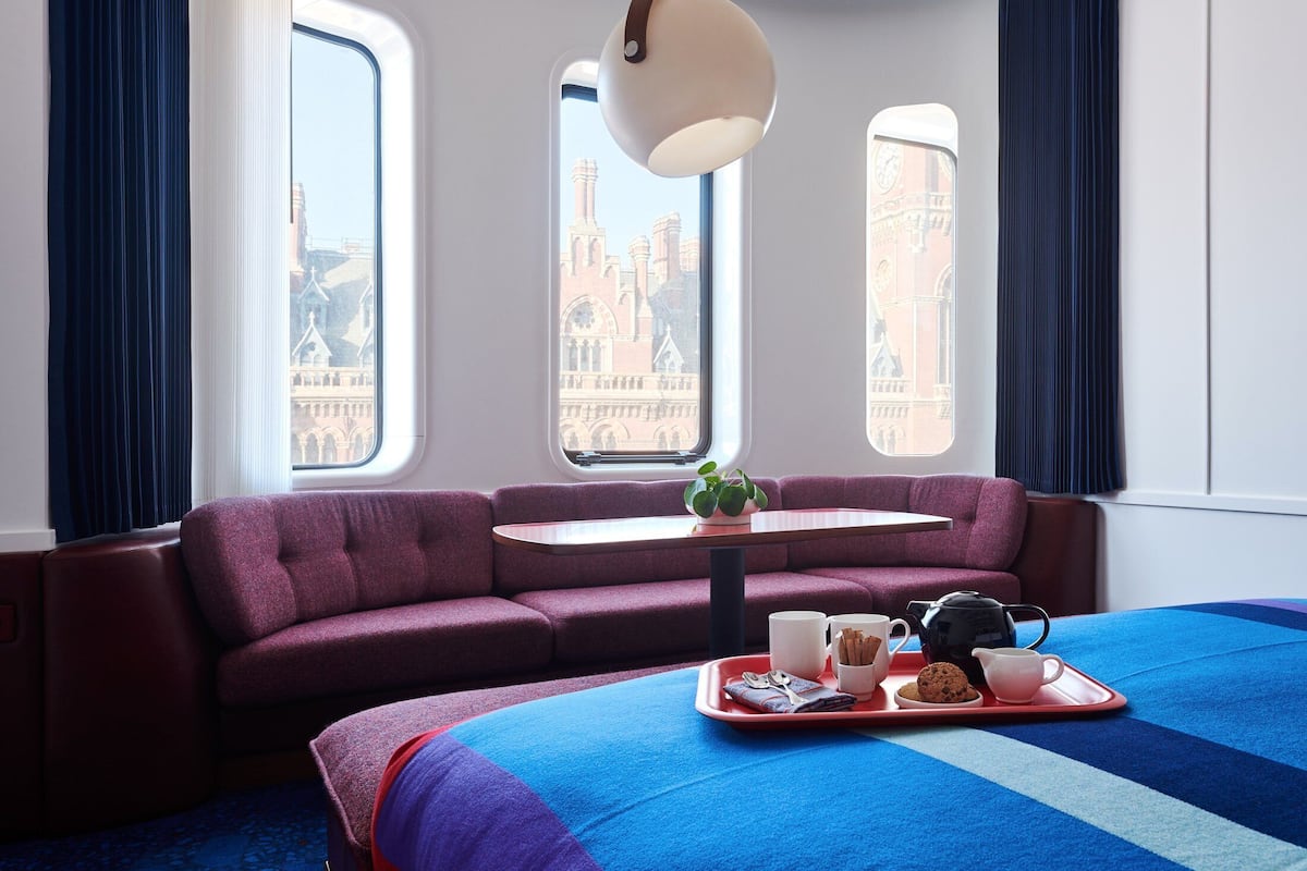 A hotel room with a large bed, a purple sofa, a small table, and a tray with breakfast items.