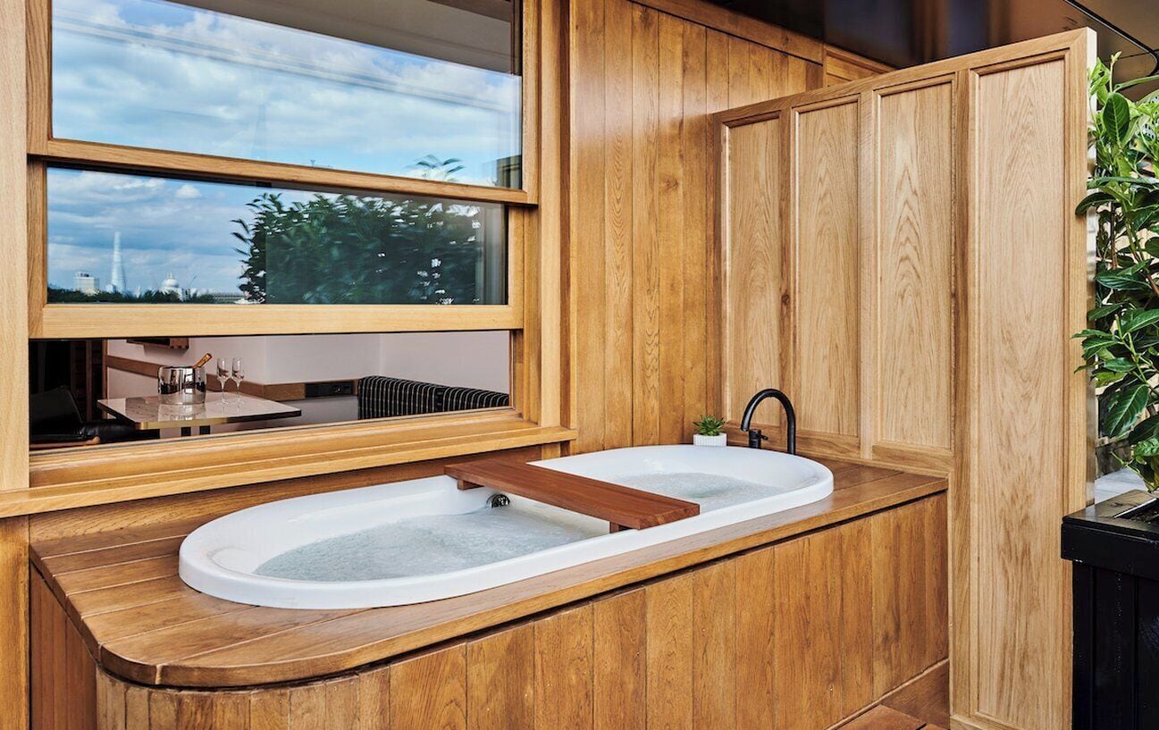 A modern bathroom with a wooden vanity, a large window, and a built-in bathtub.