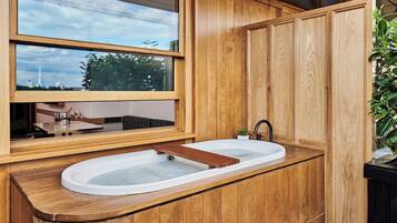 A modern bathroom with a wooden vanity, a large window, and a built-in bathtub.