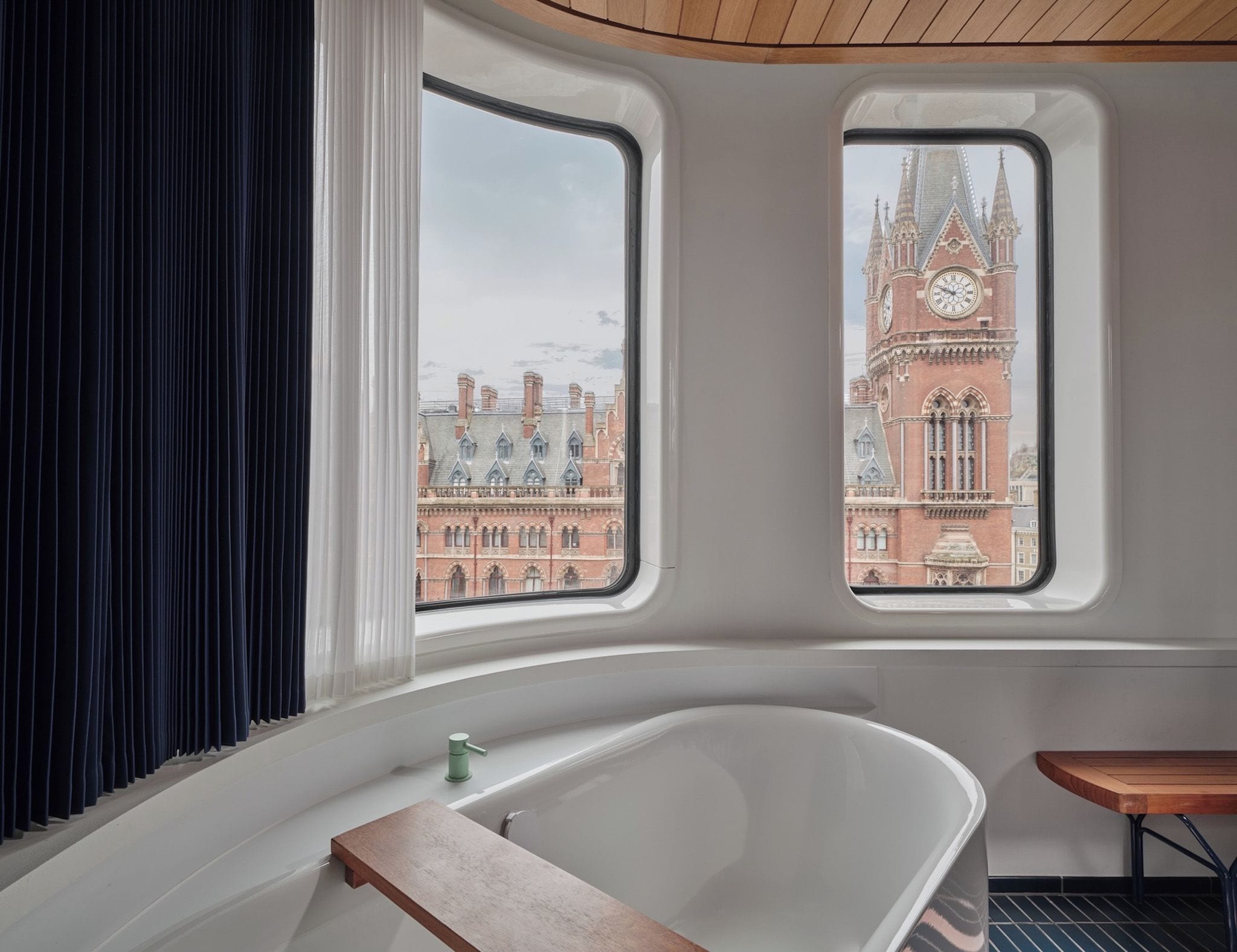 A modern bathroom with a freestanding bathtub, two large windows offering views of a historic building with a clock tower.