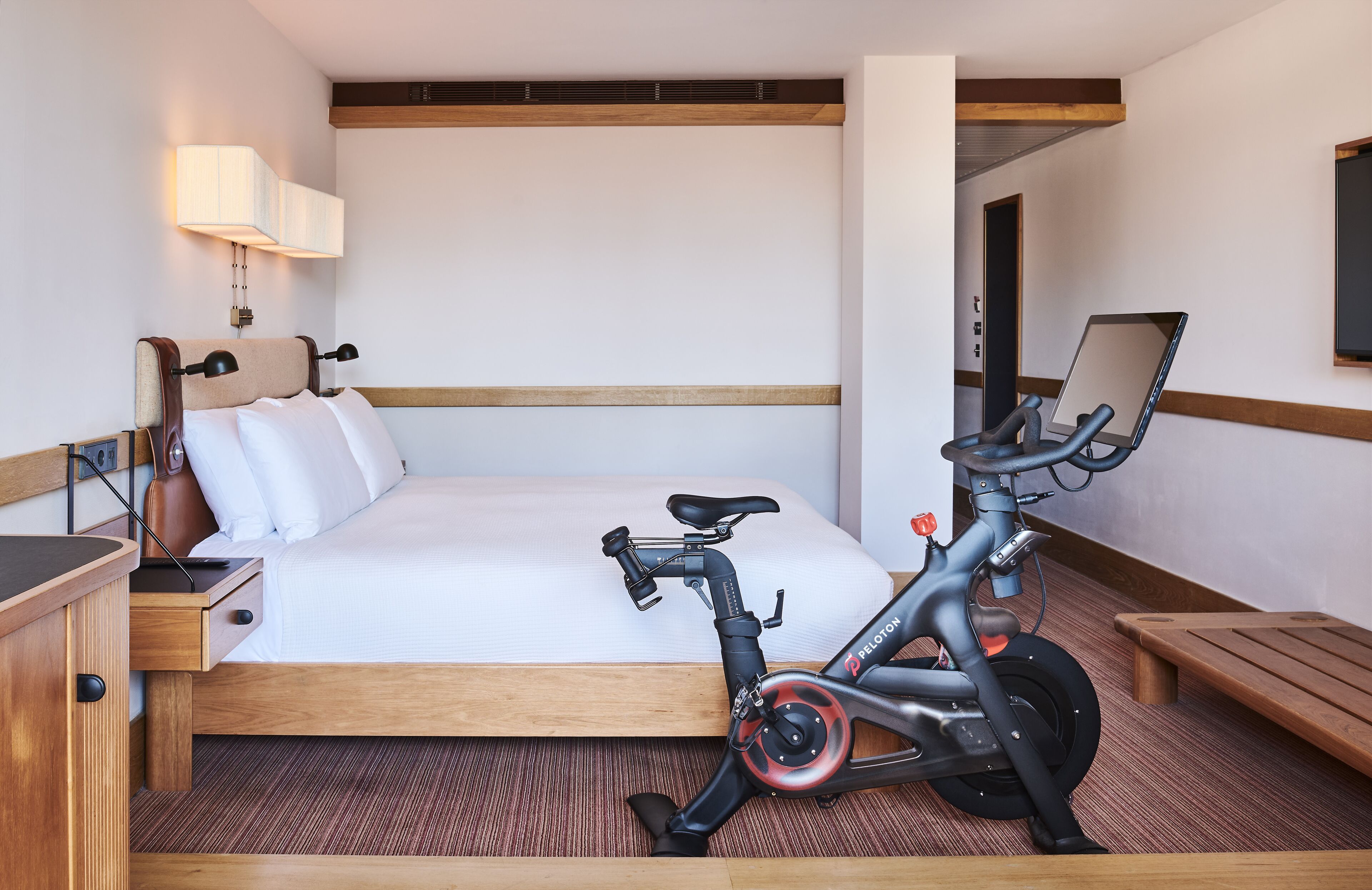 Una camera d'albergo con un letto, una scrivania, un computer portatile e una cyclette.