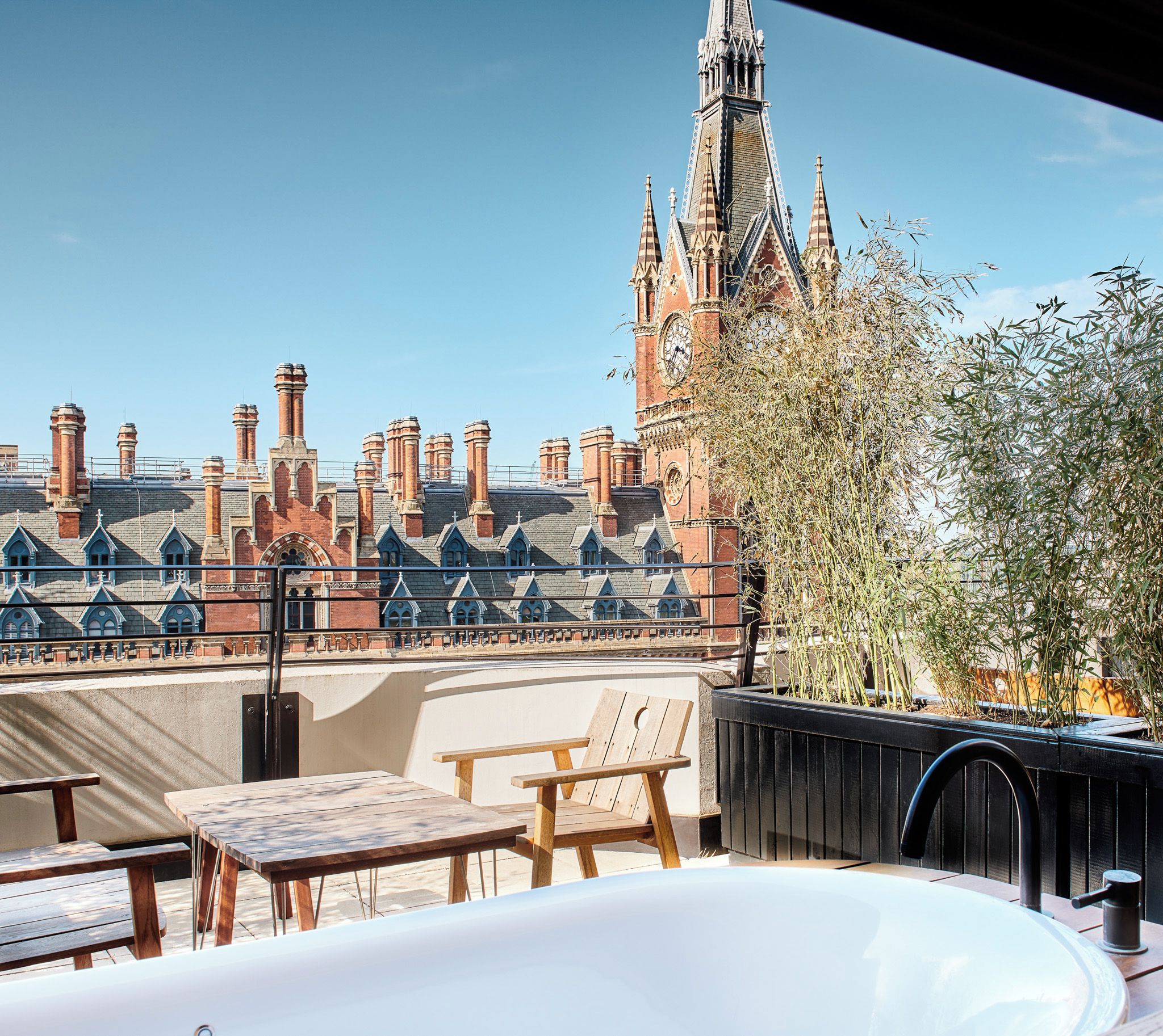 Una terraza en la azotea con vistas a un edificio histórico con varias chimeneas y una torre del reloj.