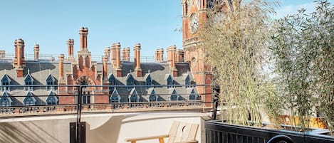 Una terraza en la azotea con vistas a un edificio histórico con varias chimeneas y una torre del reloj.