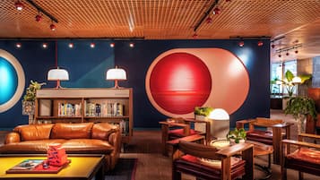 A modern lounge area with leather sofas, wooden tables, and bookshelves.