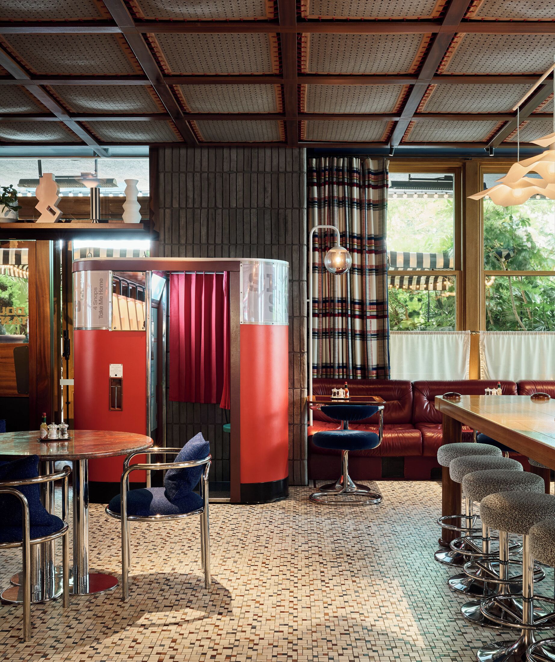 A cozy interior with a red and white booth, a bar area with stools, and a large window with a view of greenery.