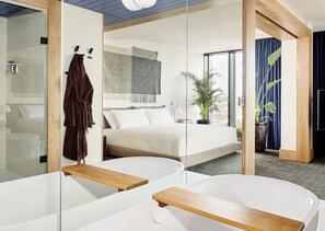 A modern hotel room with a large bed, a bathtub, and a large mirror.