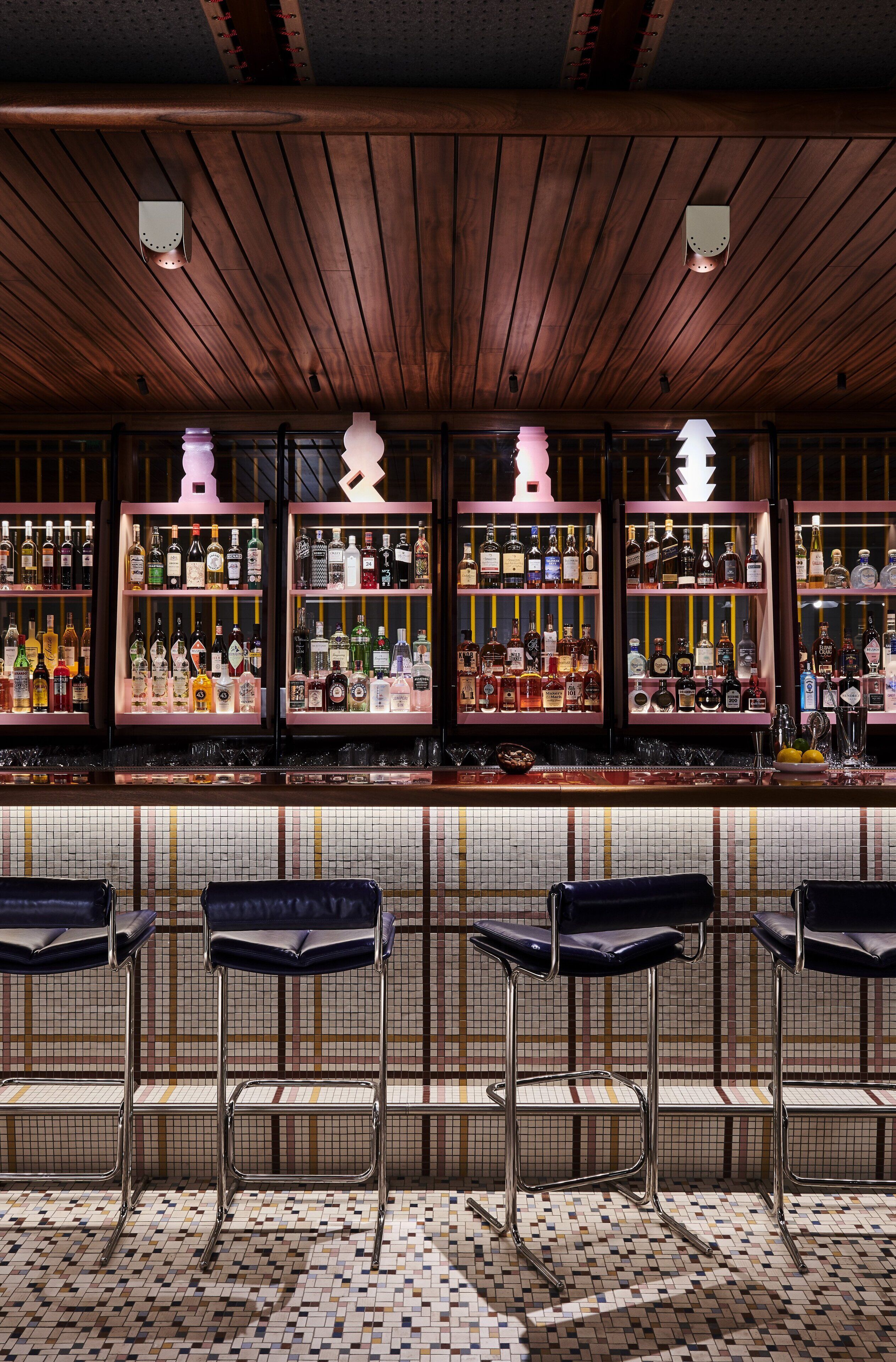 A bar area with wooden ceiling, tiled floor, and multiple shelves of liquor bottles.