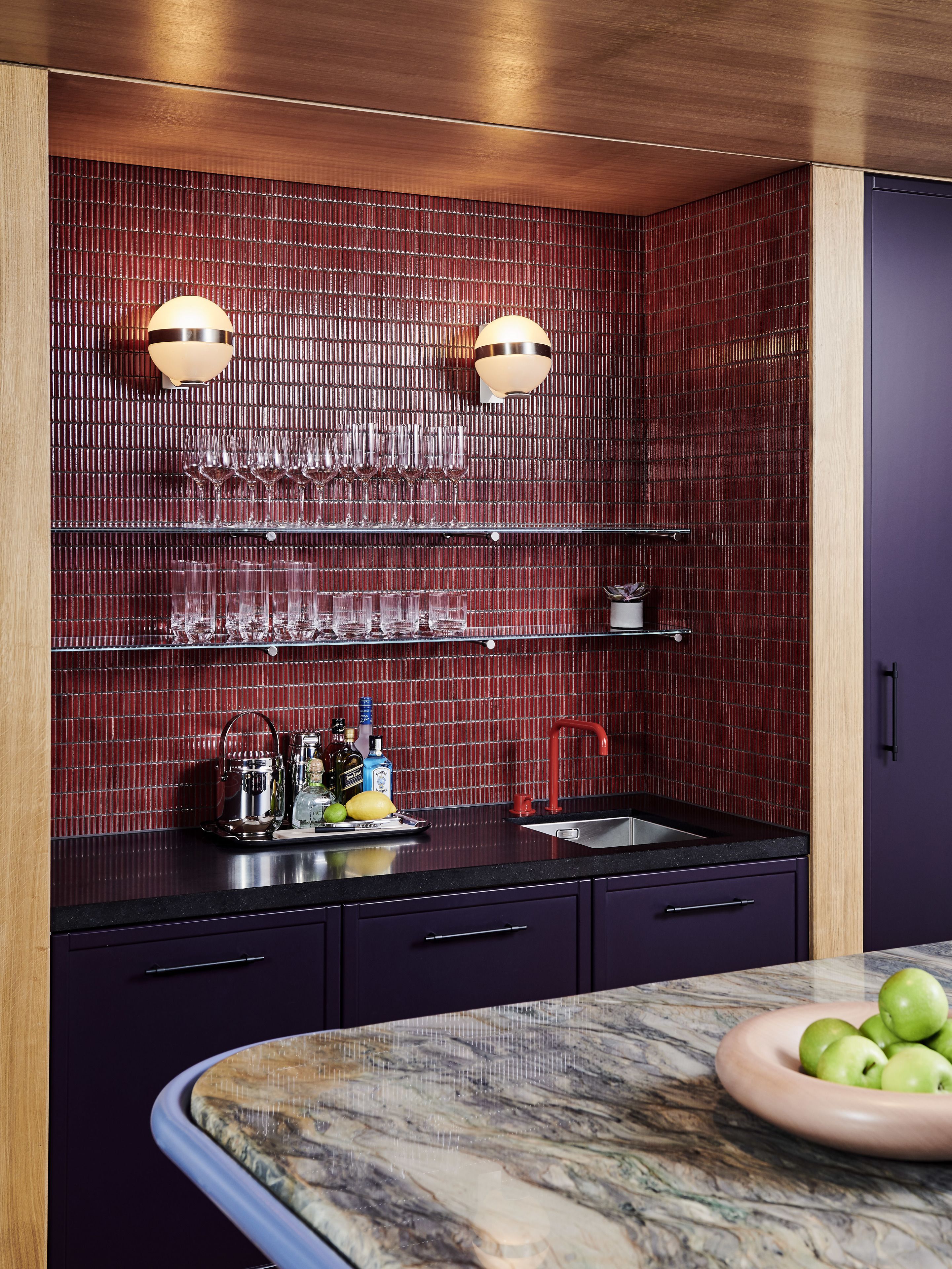 A modern kitchen with a red tiled backsplash, black countertops, and a marble island.