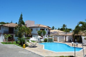 A swimming pool surrounded by buildings with tiled roofs, outdoor seating, and palm trees.