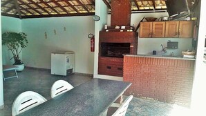 Une terrasse extérieure avec un four en briques, une table, des chaises et un téléviseur fixé au mur.