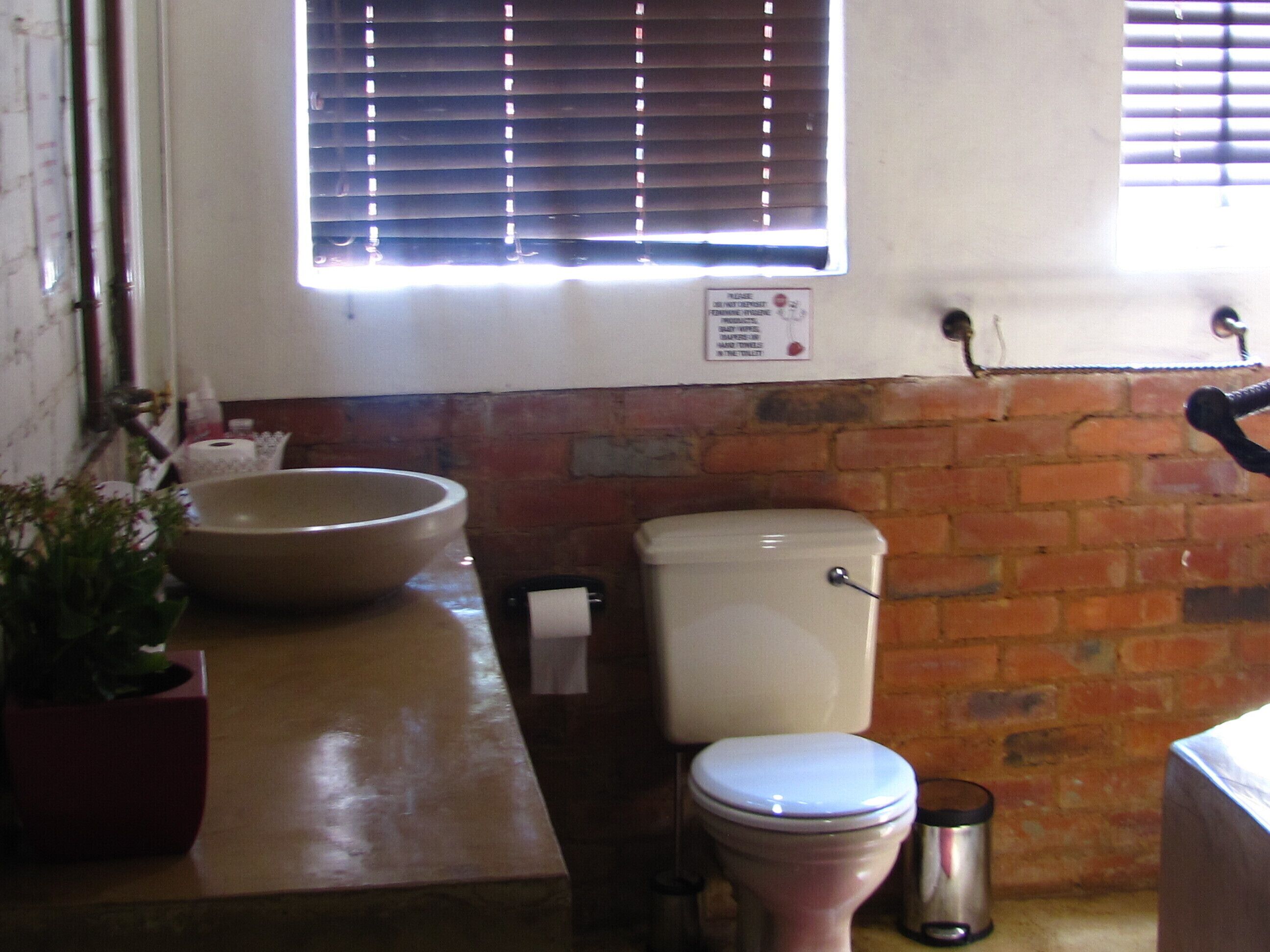 A bathroom with a large bowl sink, toilet, and a window with blinds.